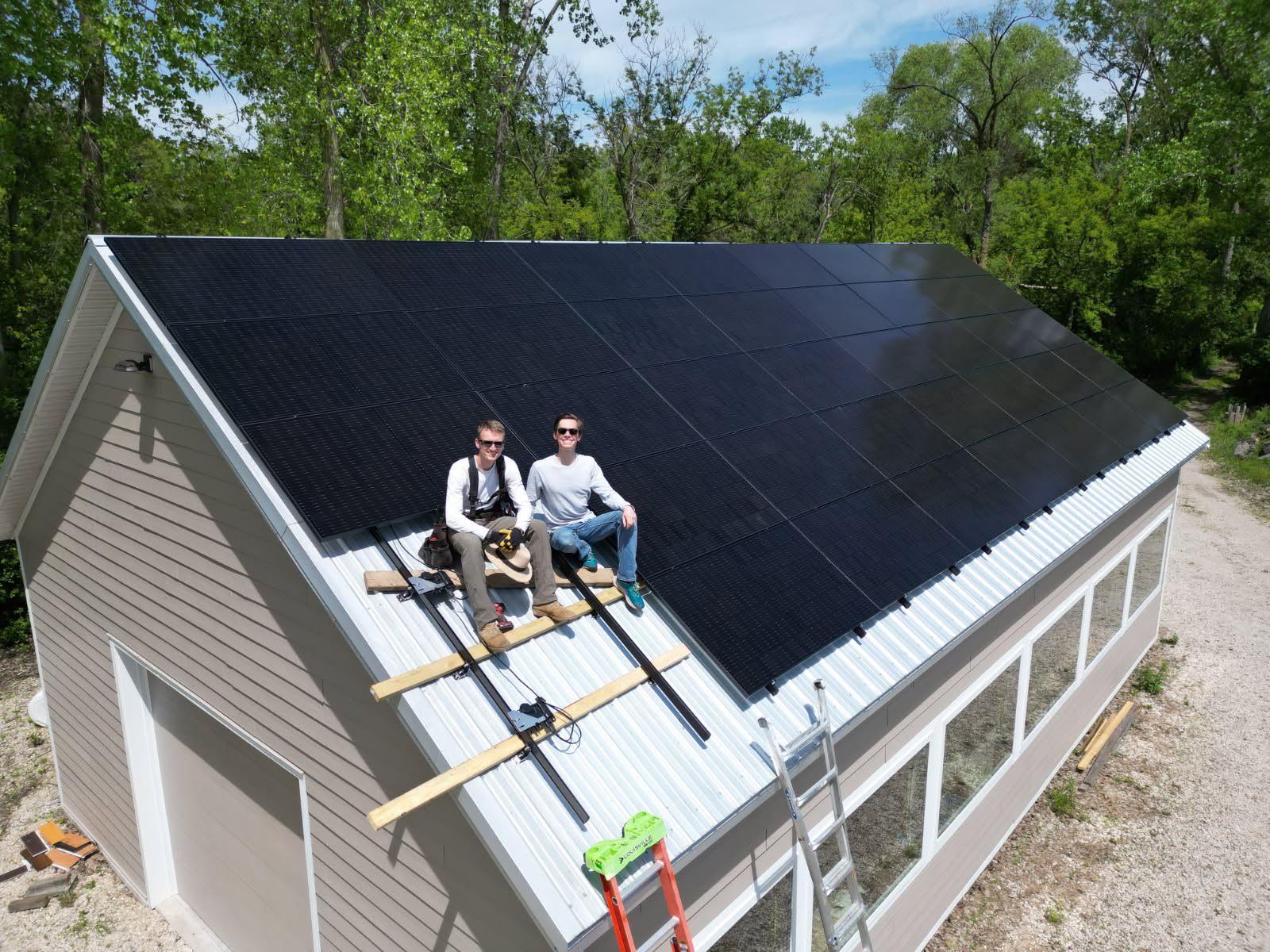 Two of the Augustine Solar team sitting on a finished metal-roof array on a West Michigan job site